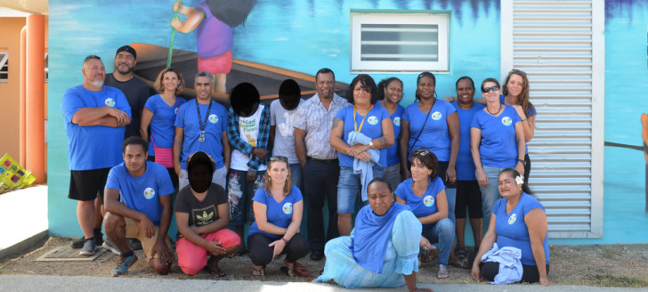 Didier Poidyaliwane et l’équipe du FAEN, dont sa directrice Karen Vernière (1er rang, 2e à droite), devant la fresque réalisée par les jeunes à l’occasion de l’anniversaire du foyer.